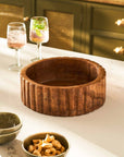 Wooden bowl on a kitchen counter with glasses and snacks