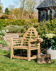 Wooden garden bench in a lush garden setting with greenery and a small building.