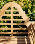 Wooden garden bench with lattice backrest against a green bush background