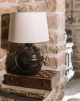 Large brown Table Lamp With Linen Shade on wooden chess board against stone wall.