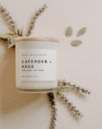Lavender and sage white soy candle with lid and herbs behind. with wooden