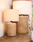 Pair of lamps with neutral rope effect base and light linen shade. Both switched on, on wooden console table.
