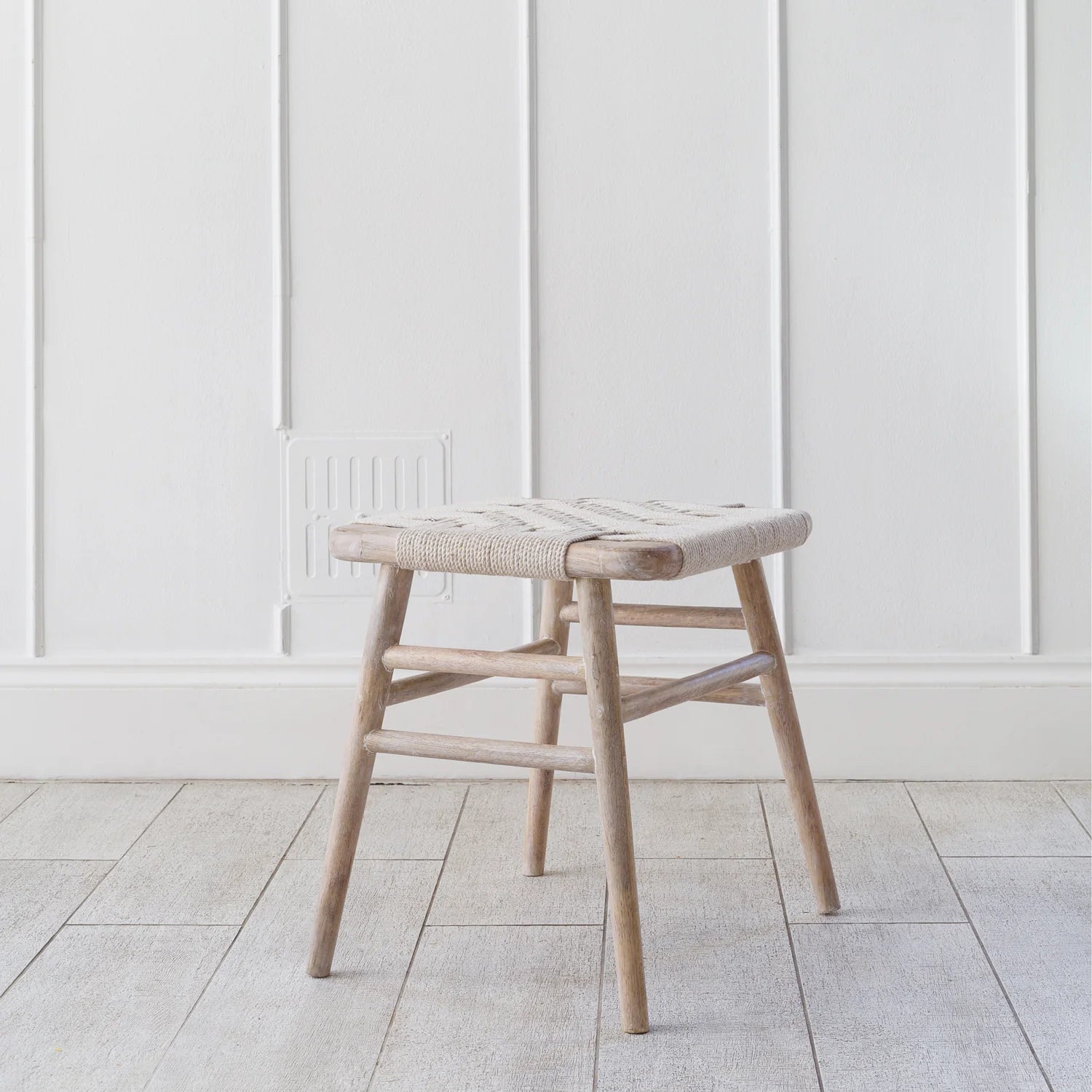 Lulworth Rustic Wooden Stool against a white panelled wall an wooden floor.