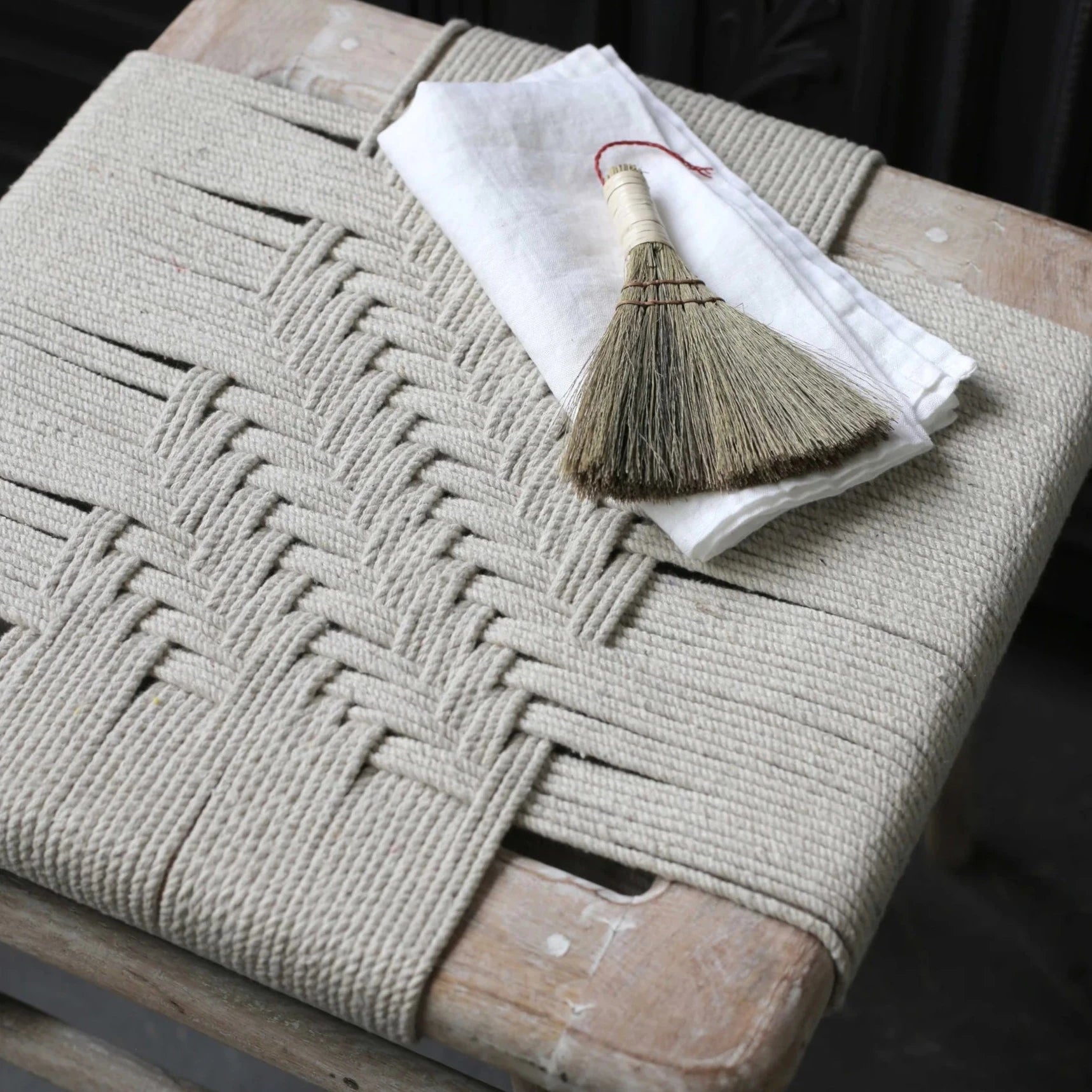 Lulworth Rustic Wooden Stool with rope seat and white napkin with straw brush on top.