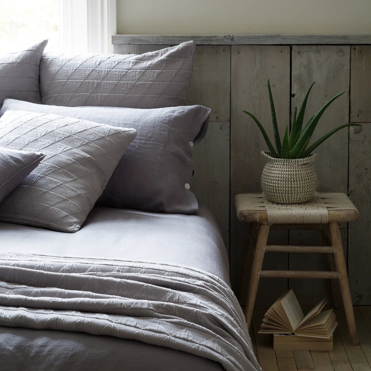 A rustic bedroom with lilac bedding, wooden cladded walls and the Lulworth Rustic Wooden Stool as a bedside table.