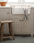 A neutral shaker style kitchen with white sink and small rustic wooden stool.