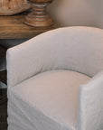 close up image of Natural linen dining chair with rounded back next to a wooden side table.