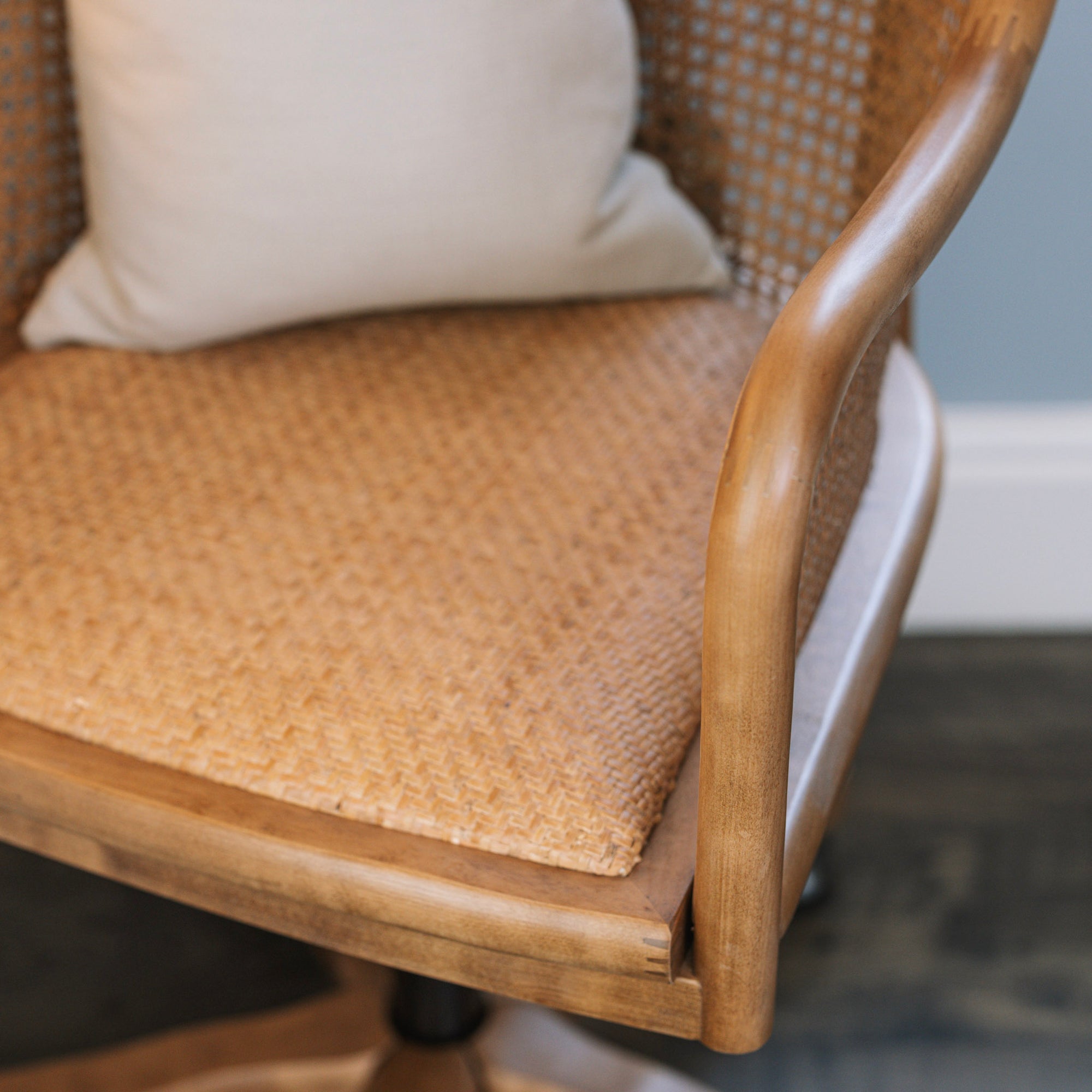 Natural rattan wicker office chair with neutral cushion at white desk.