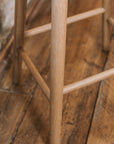 Natural wooden backless barstool against stone wall, shot of the leg.