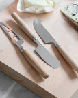Cheese knife set of three on wooden chopping board with cheese.