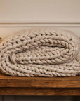 Chunky cream knitted blanket folded up on console.