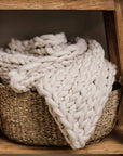 Chunky knitted blanket rolled up in a woven wicker basket.