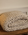 Chunky knit blanket folded up on a wooden console side view.