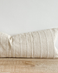 Close up of cream bolster cushion with embroidered stripes on wooden surface.