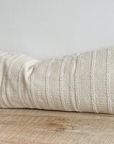 Cream bolster cushion with embroidered stripes on wooden surface.