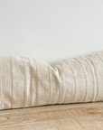 Cream bolster cushion with embroidered stripes on wooden surface.