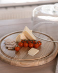glass and wood cake dome with cheese, tomatoes and crackers on wooden table.