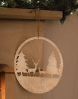 Reindeer scene hanging decoration, hanging from a fireplace mantel with a garland.