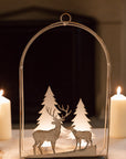 White reindeer forest scene hanging wall decor with lit tealights in, on a table with dinner candles behind.