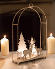 White reindeer forest scene hanging wall decor with lit tealights in, on a table with dinner candles behind.