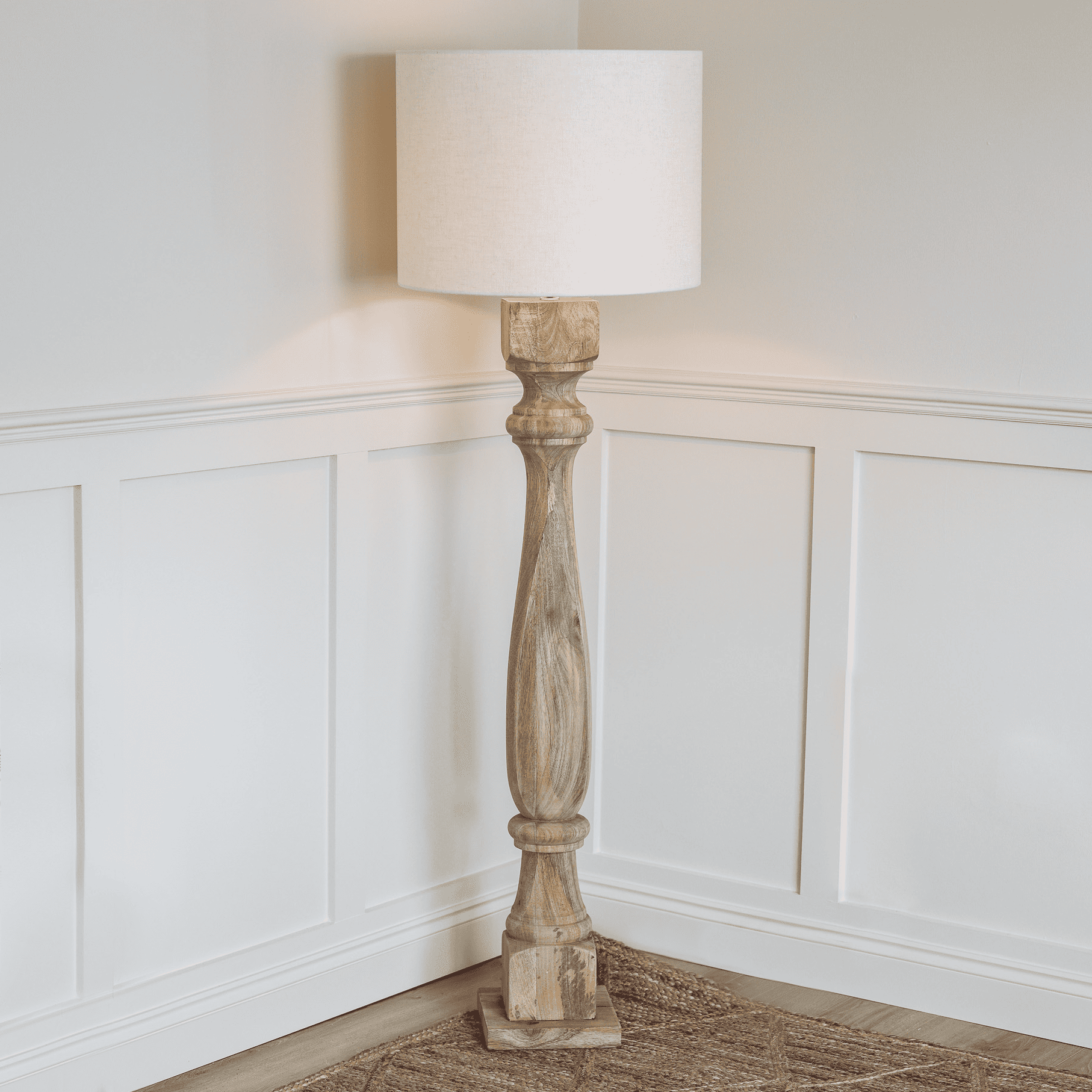 Tall wooden floor lamp switched on in the corner of a room.