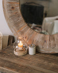 Rustic Round Wooden Mirror on wooden table with small candle and pot of matches.