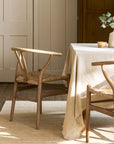 Dining room with wishbone dining chairs and a table covered with a beige tablecloth.