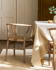 Wooden wishbone dining chairs with woven seat next to a table with a beige tablecloth in a room with wooden paneling.