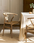 Dining room with wishbone dining chairs and a table covered with a beige tablecloth.