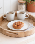 Round wooden tray with two cream coffee mugs and a pastry.