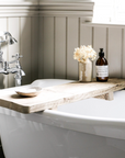 A chunky reclaimed bath board with a soap bottle and small vase with dried flowers in a bathroom.