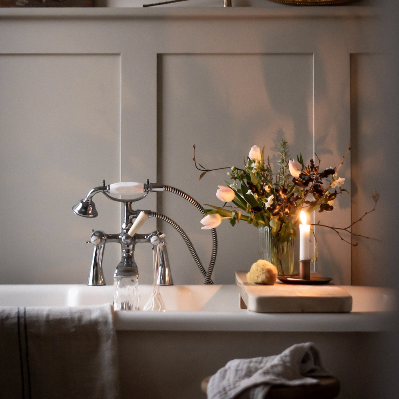 A free standing bath with the tap running and a rustic bath board sitting ontop of the bath  with fresh flowers and a candle.