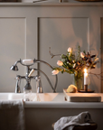 A free standing bath with the tap running and a rustic bath board sitting ontop of the bath with fresh flowers and a candle.