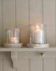A set of two rustic glass candle holder against a panelled wall.