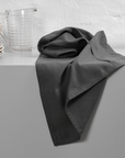 Dark grey towel scrunched on a surface with plates and a glass jug.