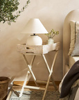 Rattan tray table next to bed with lamp and vase inside.