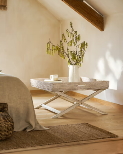 Rattan tray coffee table in bedroom with plant and mug on.