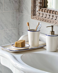 White and blue toothbrush holder with toothbrushes, and soap dispenser on bathroom sink.