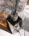 Large amber reed diffuser with presentation box on stone hearth.