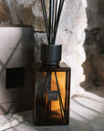 Large amber reed diffuser with presentation box on stone hearth.