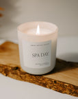 Large matt white soy candle, lit on a plank of wood.