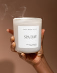 Large matt white soy candle, held up in one hand with blown out smoke coming off.