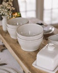 white cereal bowls on wooden serving plank with butter dish and flowers.