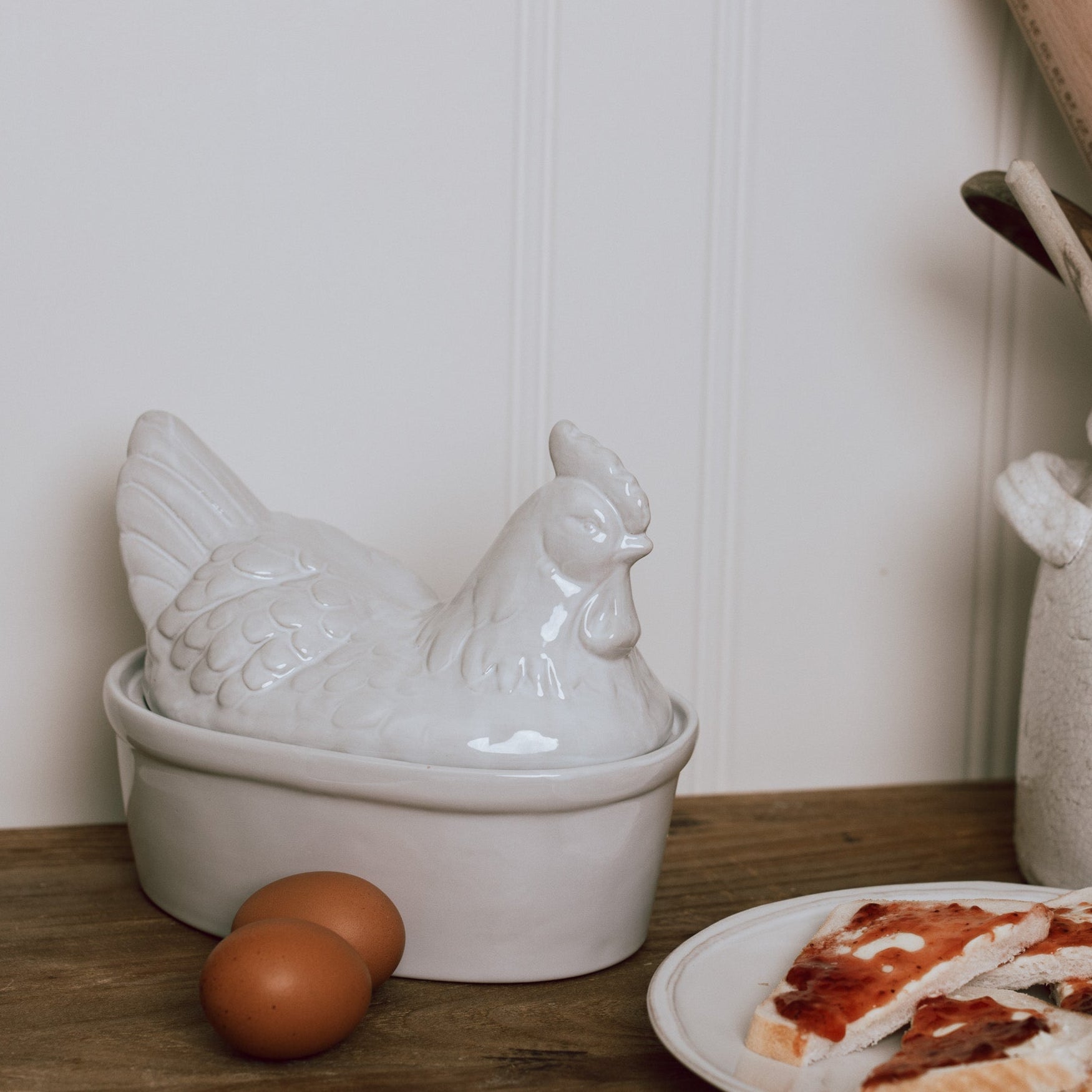 White Ceramic Egg Holder shades like a chicken with two eggs on a wooden chopping board.