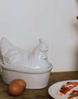 White Ceramic Egg Holder shades like a chicken with two eggs on a wooden chopping board.
