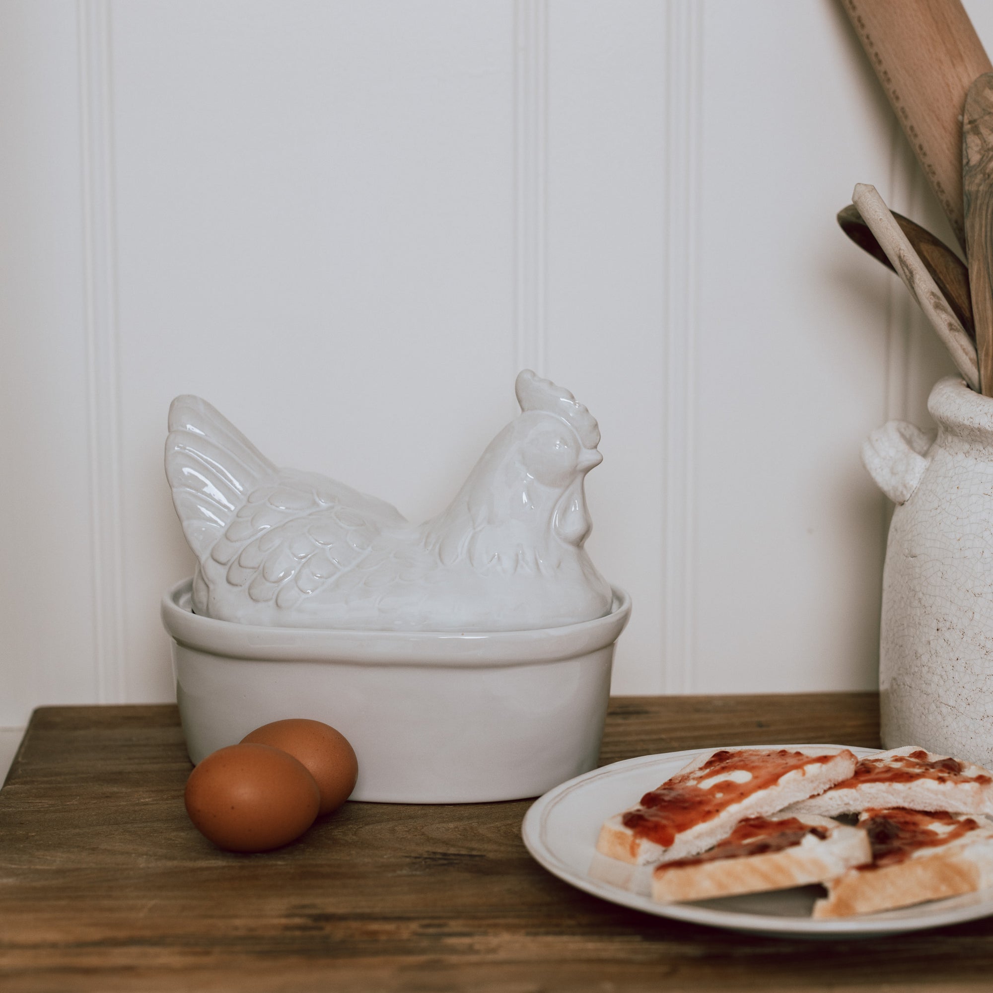 White Ceramic Egg Holder shades like a chicken with two eggs on a wooden chopping board.