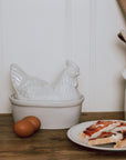 White Ceramic Egg Holder shades like a chicken with two eggs on a wooden chopping board.