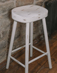 White washed rustic wooden bar stool against stone wall.