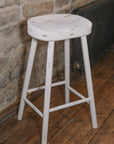 White washed rustic wooden bar stool against stone wall.
