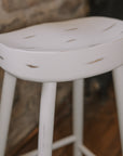 detailed shot of White washed rustic wooden bar stool against stone wall.
